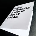 Close-up angled view of greeting card with bold black text reading “Have Yourself a Holly Jolly Xmas.”