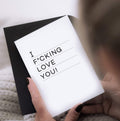 Person holding white card with black text “I f*cking love you” and black envelope visible