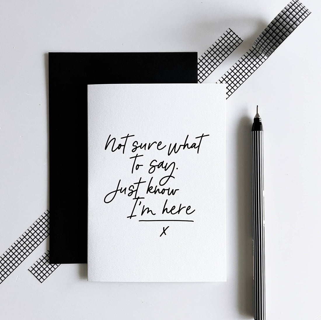 White sympathy card with black text “Not sure what to say. Just know I’m here” beside black envelope.