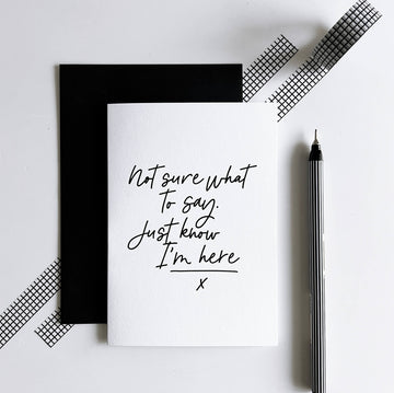 White sympathy card with black text “Not sure what to say. Just know I’m here” beside black envelope.