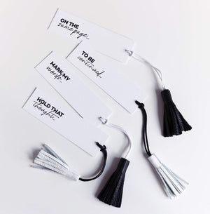 Set of four white bookmarks with black and white leather tassels and witty phrases