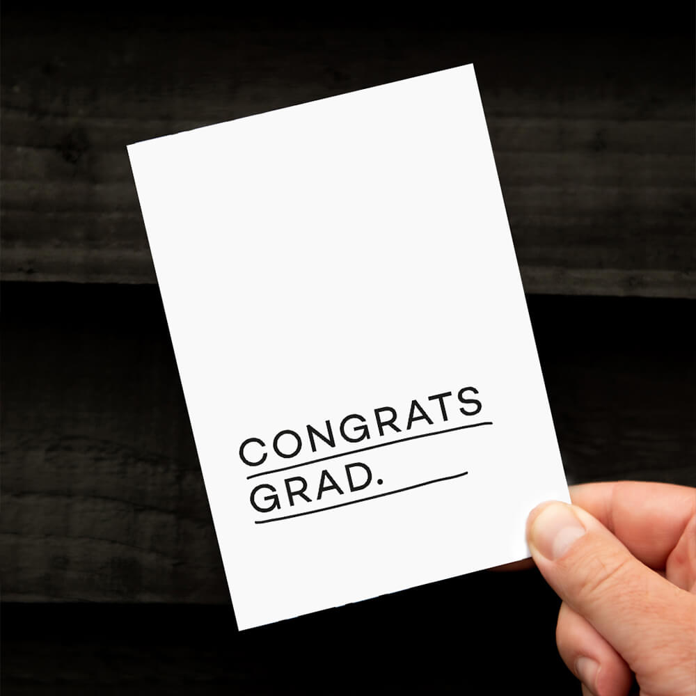 Hand holding a minimal white graduation card with bold Congrats Grad text.