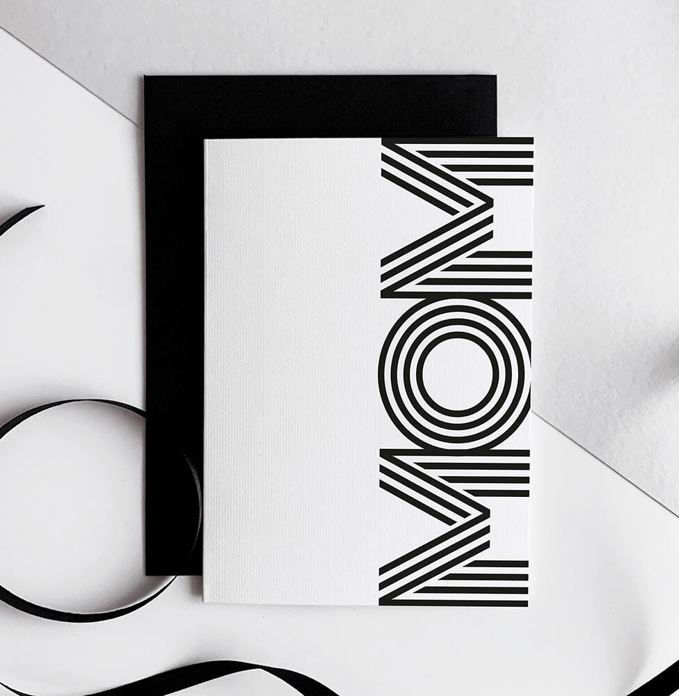 White birthday card with bold black "MOM" text, black envelope beside it.