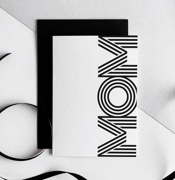 White birthday card with bold black "MOM" text, black envelope beside it.