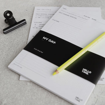 HELLO TIME My Day Desk Pad with black cover band and yellow pencil on grey desk