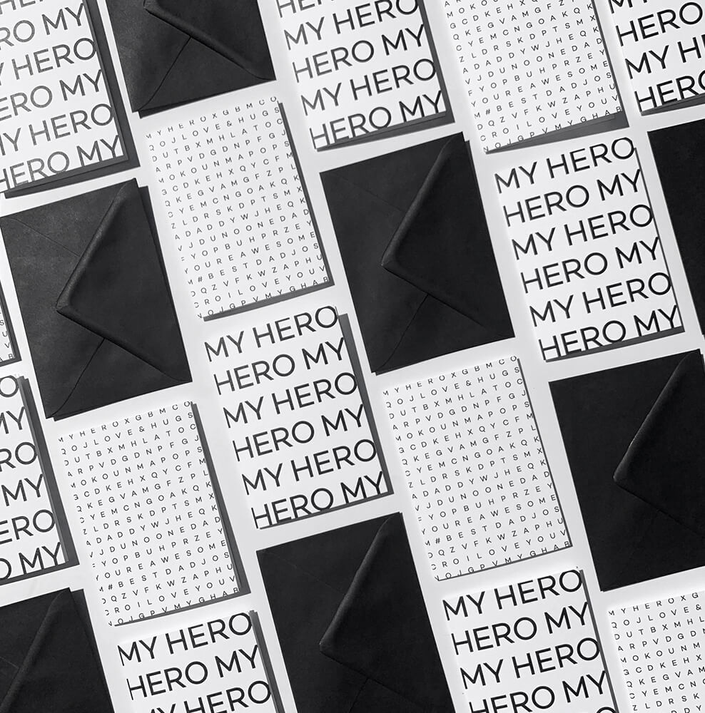 Flat lay of multiple My Hero Dad birthday cards with matching black envelopes.