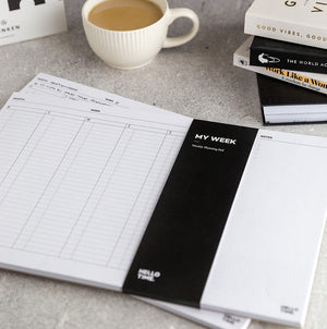 Hello Time My Week Planning Desk Pad in monochrome, open on a desk with coffee, books, and minimalist layout visible