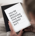 Person holding New Parents greetings card with black text on white card and black envelope.