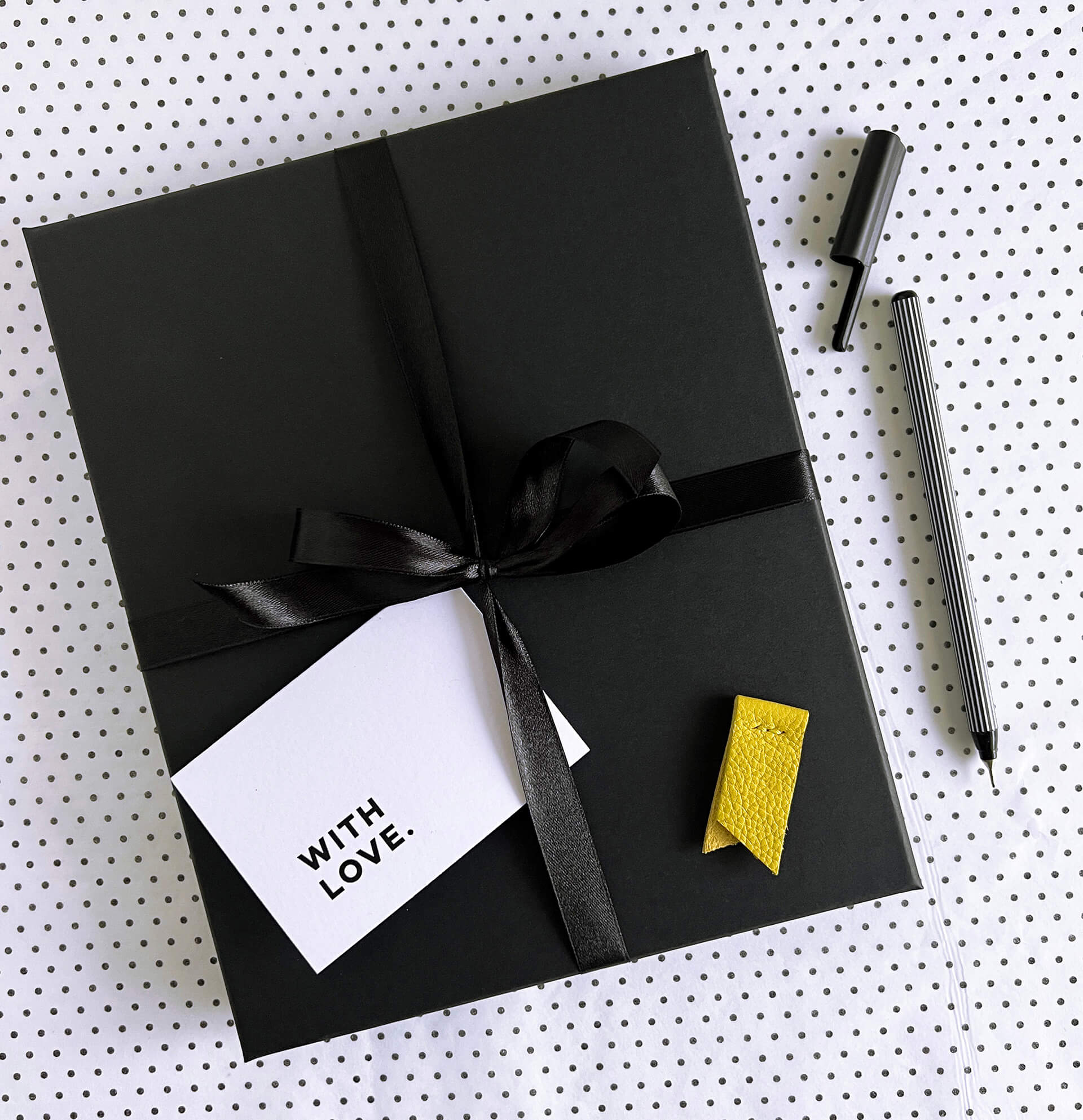 Wrapped black gift box with black ribbon, gift card, yellow marker, and black striped pen