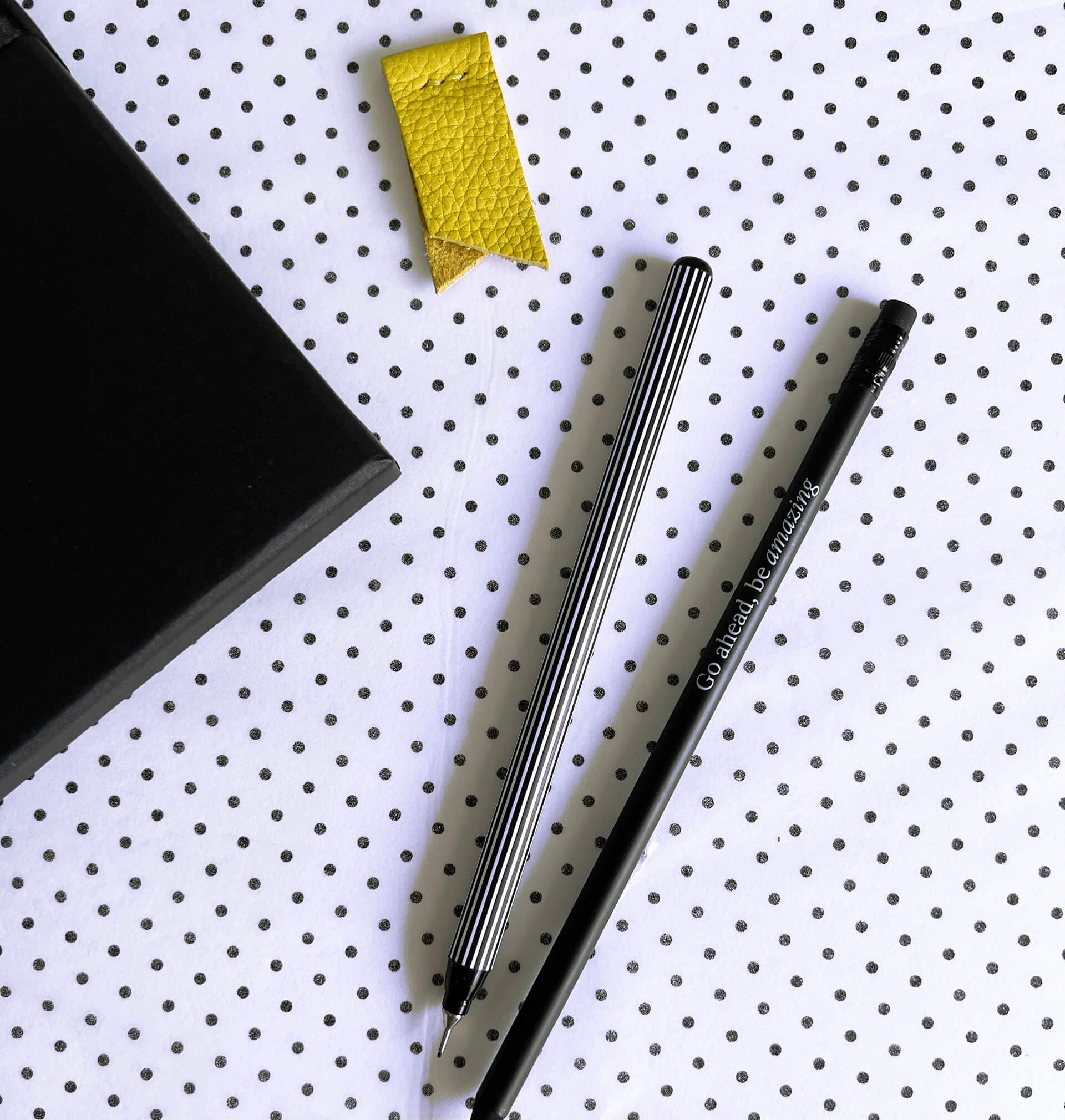 Yellow page marker, striped fineliner, black pencil and notebook corner from stationery gift set on dotted background