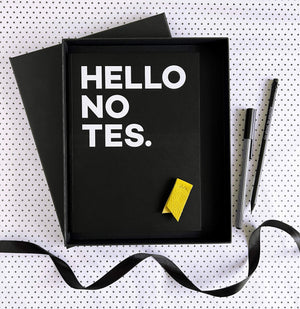 Open black gift box with HELLO NOTES notebook, yellow leather marker, pencil and pen on spotty paper