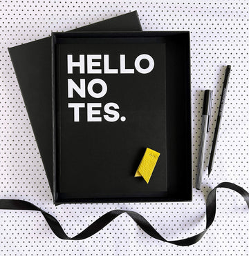 Open black gift box with HELLO NOTES notebook, yellow leather marker, pencil and pen on spotty paper