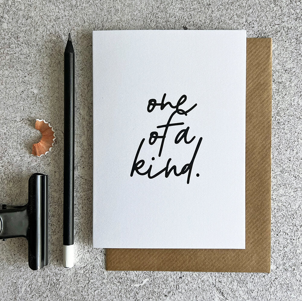 White birthday card with handwritten text "one of a kind" in black, paired with a brown kraft envelope.