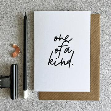 White birthday card with handwritten text "one of a kind" in black, paired with a brown kraft envelope.