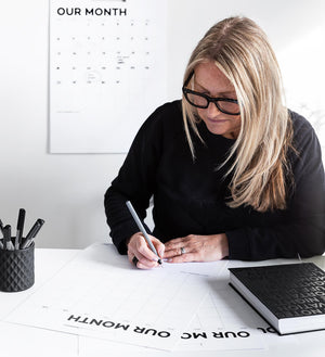 Woman writing on Hello Time monthly planner sheets at white desk with pen pot and black notebook