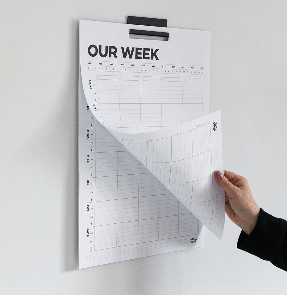 Person placing Hello Time weekly family wall planner on kitchen wall near open shelf with dishes and boards