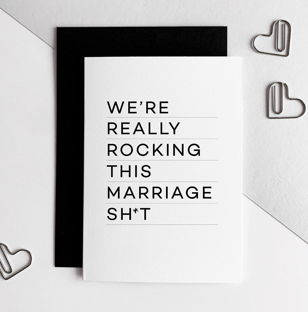 White anniversary card with bold black text reading "We’re really rocking this marriage sh*t," black envelope behind.
