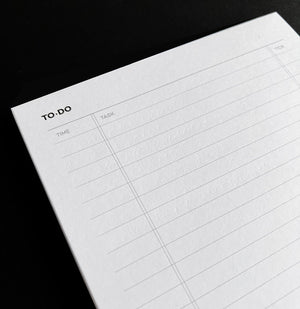 Close-up of white HELLO TIME Time Task Tick desk pad showing lined to-do layout on black background
