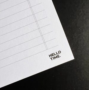 Close-up of HELLO TIME logo on white Time Task Tick desk pad with lined layout on black surface