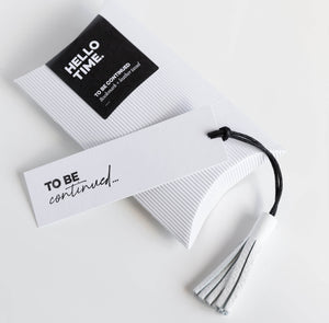 White leather tassel bookmark with “To Be Continued” card shown with branded packaging