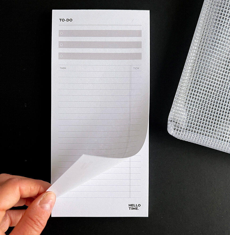 HELLO TIME Top 3 To-Do List Pad with hand turning page and mesh zip pouch on black surface

