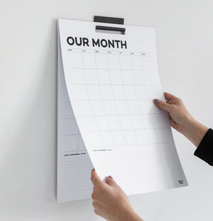 Hands turning page of black and white monthly undated wall planner mounted on wall with black mental bracket