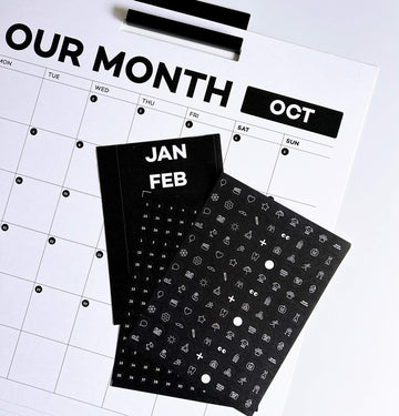 Black and white wall planner with month labels and icon stickers laid out