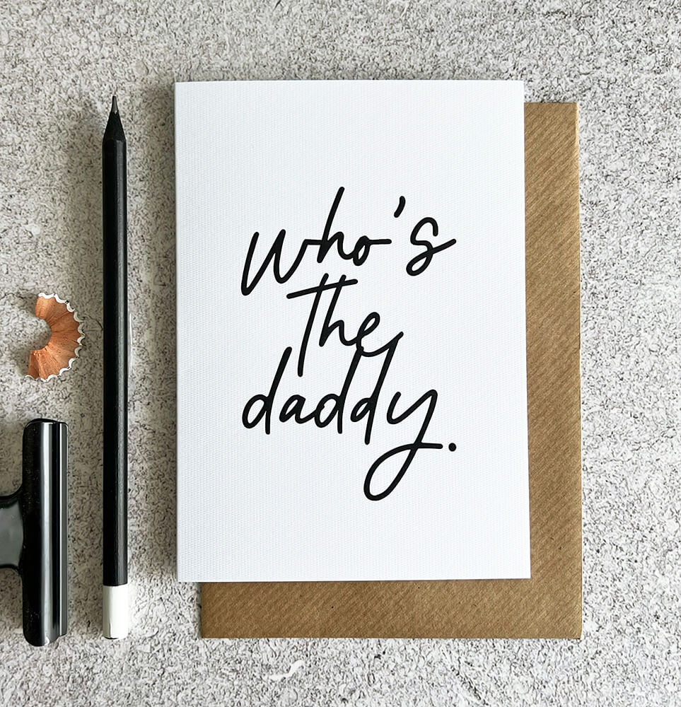 White card with black handwritten text "Who’s The Daddy" and brown kraft envelope.