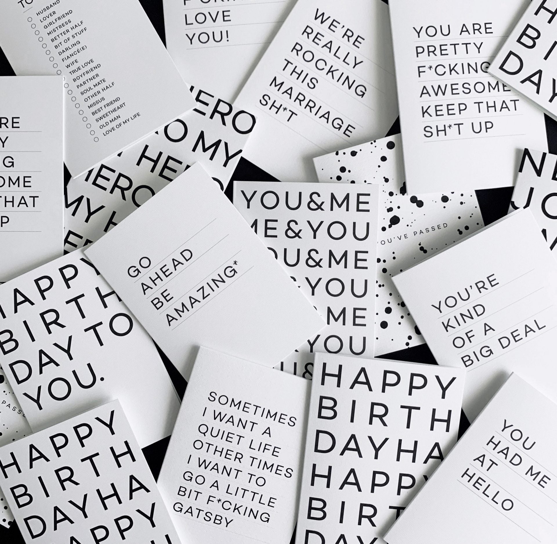 Flatlay of white greetings card with black Whoop Woo design, pen and black envelope.