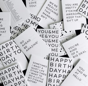 Flatlay of white greetings card with black Whoop Woo design, pen and black envelope.