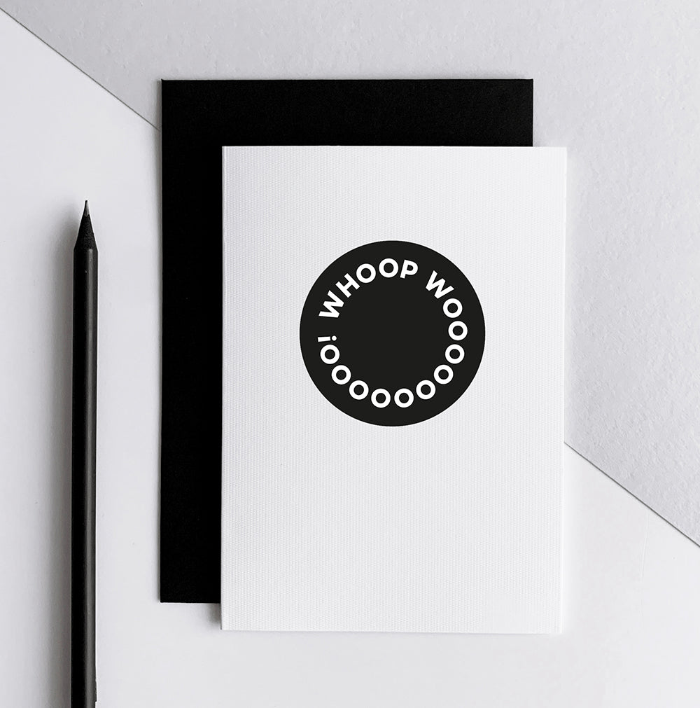 White greetings card with black circle design and Whoop Woo text, shown with black envelope.