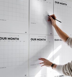 Person writing on a wall of Hello Time monthly calendar sheets with black pencil

