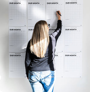 Woman writing on a full wall of blank Hello Time monthly planners in natural light