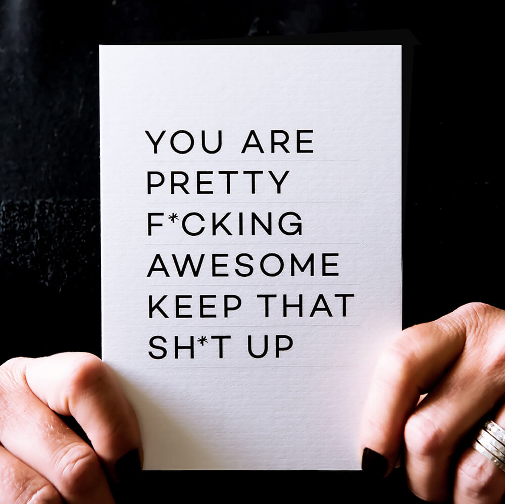 Person holding white birthday card with bold black text reading ‘You are pretty fcking awesome keep that sht up’.