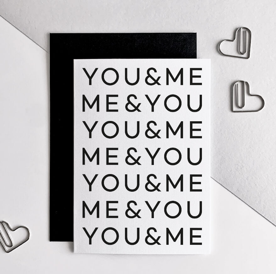 White anniversary card with repeated black text "YOU&ME ME&YOU," shown with black envelope and heart-shaped paperclips.