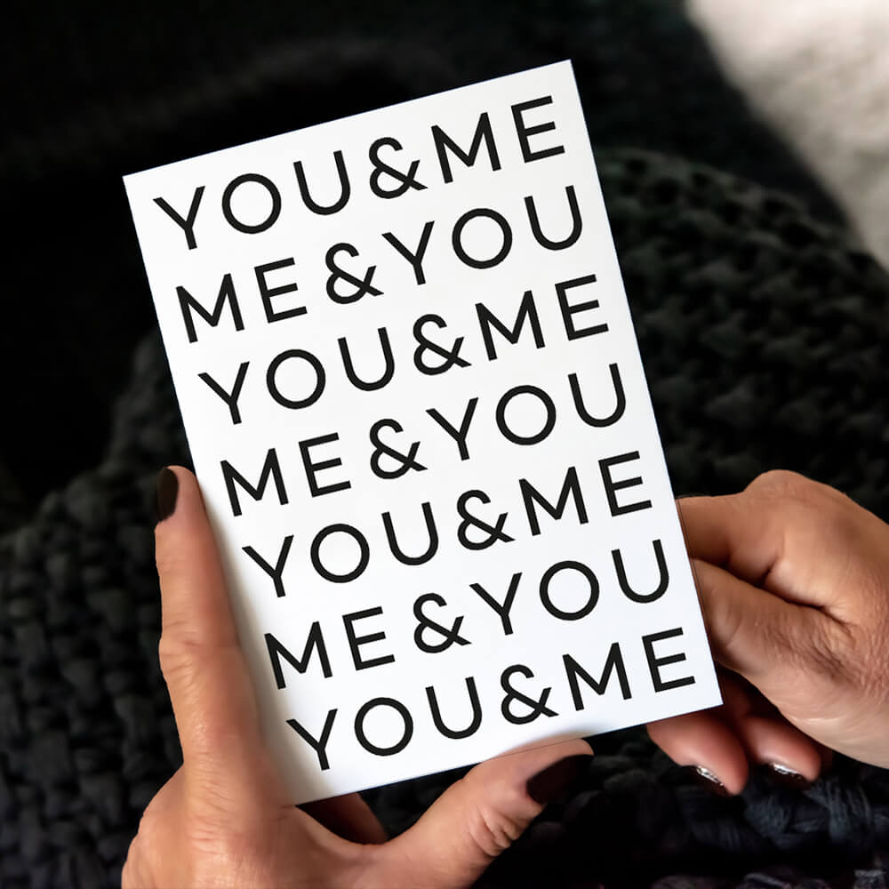 White anniversary card with repeated black text "YOU&ME ME&YOU," shown with black envelope and heart-shaped paperclips.