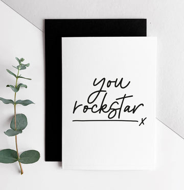 White card with black handwritten text “you rockstar” and black envelope, minimalist design.