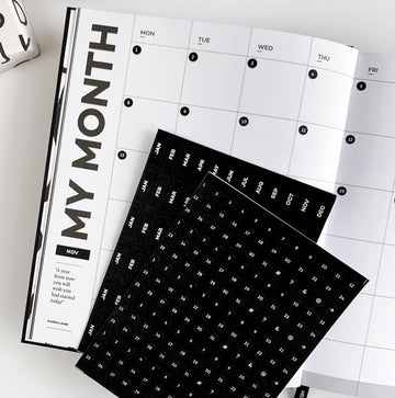 Black and white monthly planner with HELLO TIME circular date stickers on an open Month page